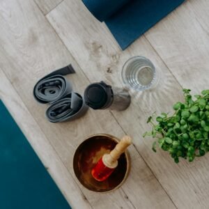 Flat lay of yoga essentials including a singing bowl, mat, plant, and hydration accessories.