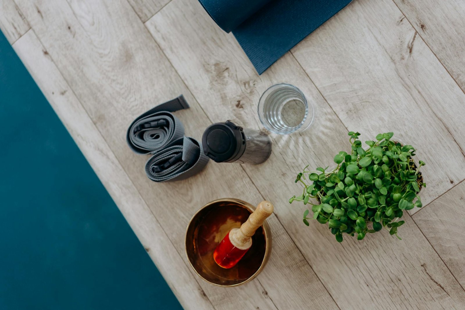 Flat lay of yoga essentials including a singing bowl, mat, plant, and hydration accessories.